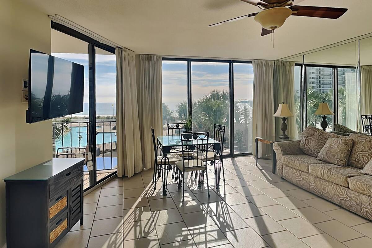 A spacious living room with a balcony, a ceiling fan, a TV, a dining table, and a sofa.