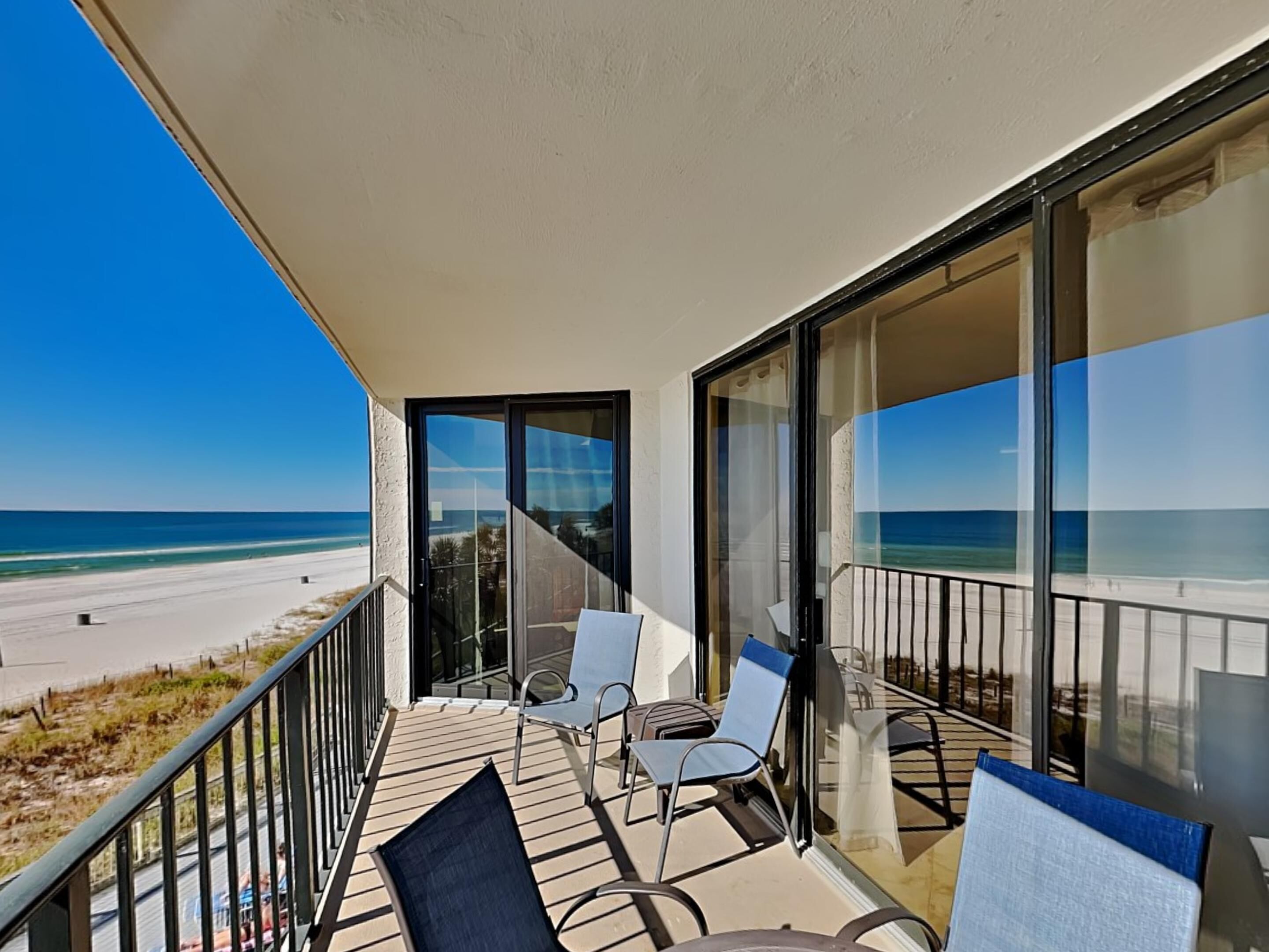 Un balcon donnant sur la plage, deux chaises et une porte vitrée.