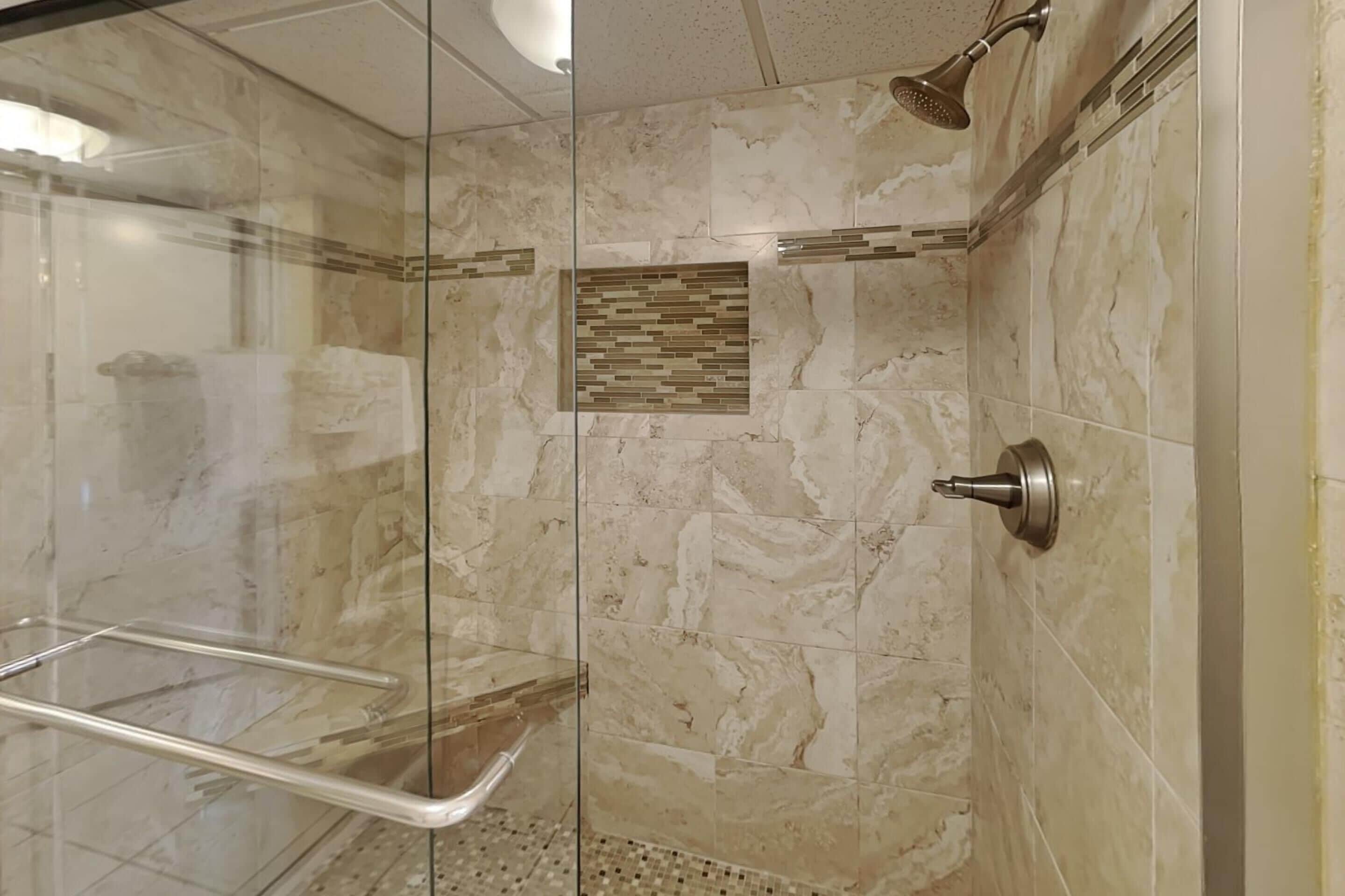 Une douche fermée par des parois de verre, avec des carreaux de marbre et un pommeau de douche.