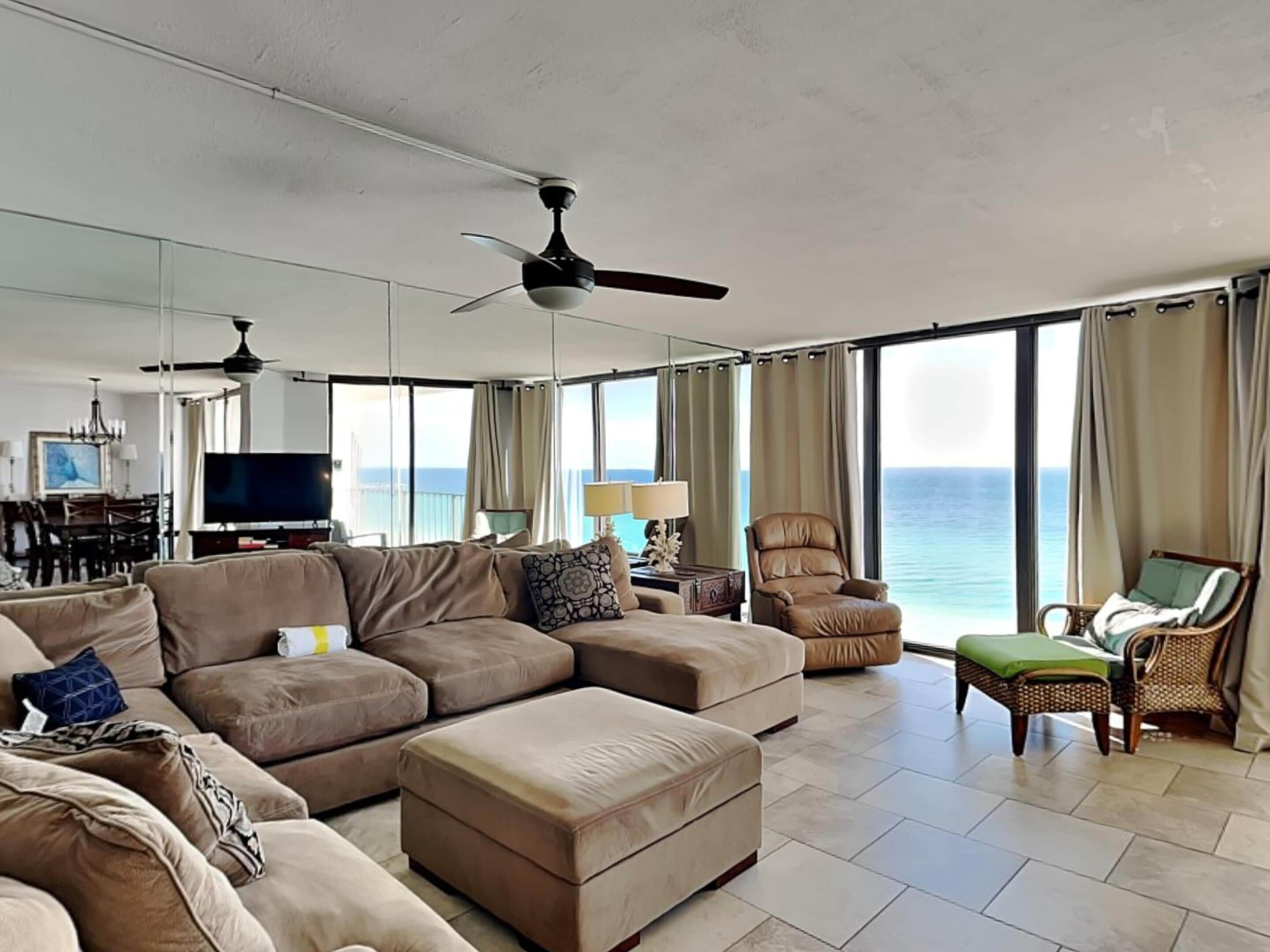 A spacious living area with a large sofa, ottoman, and a chair, a television, and a dining area with a chandelier.