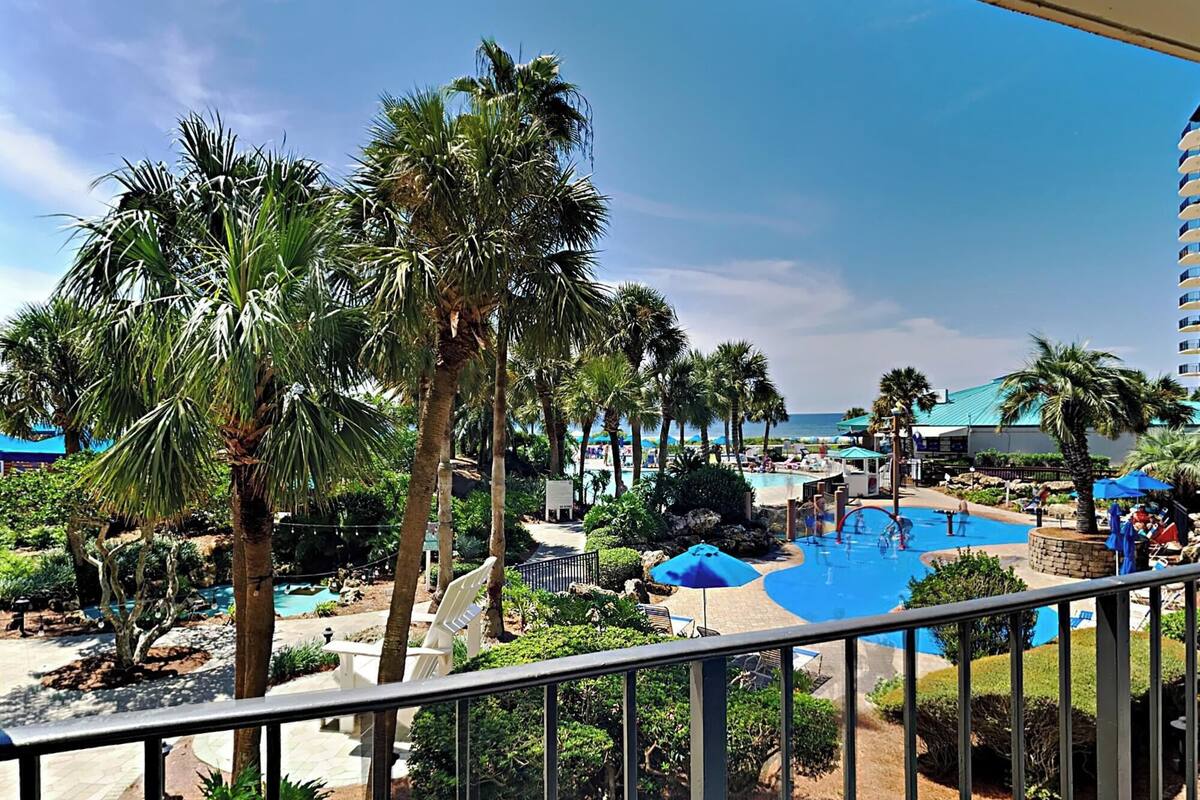 A resort with a pool area, palm trees, and a view of the ocean.