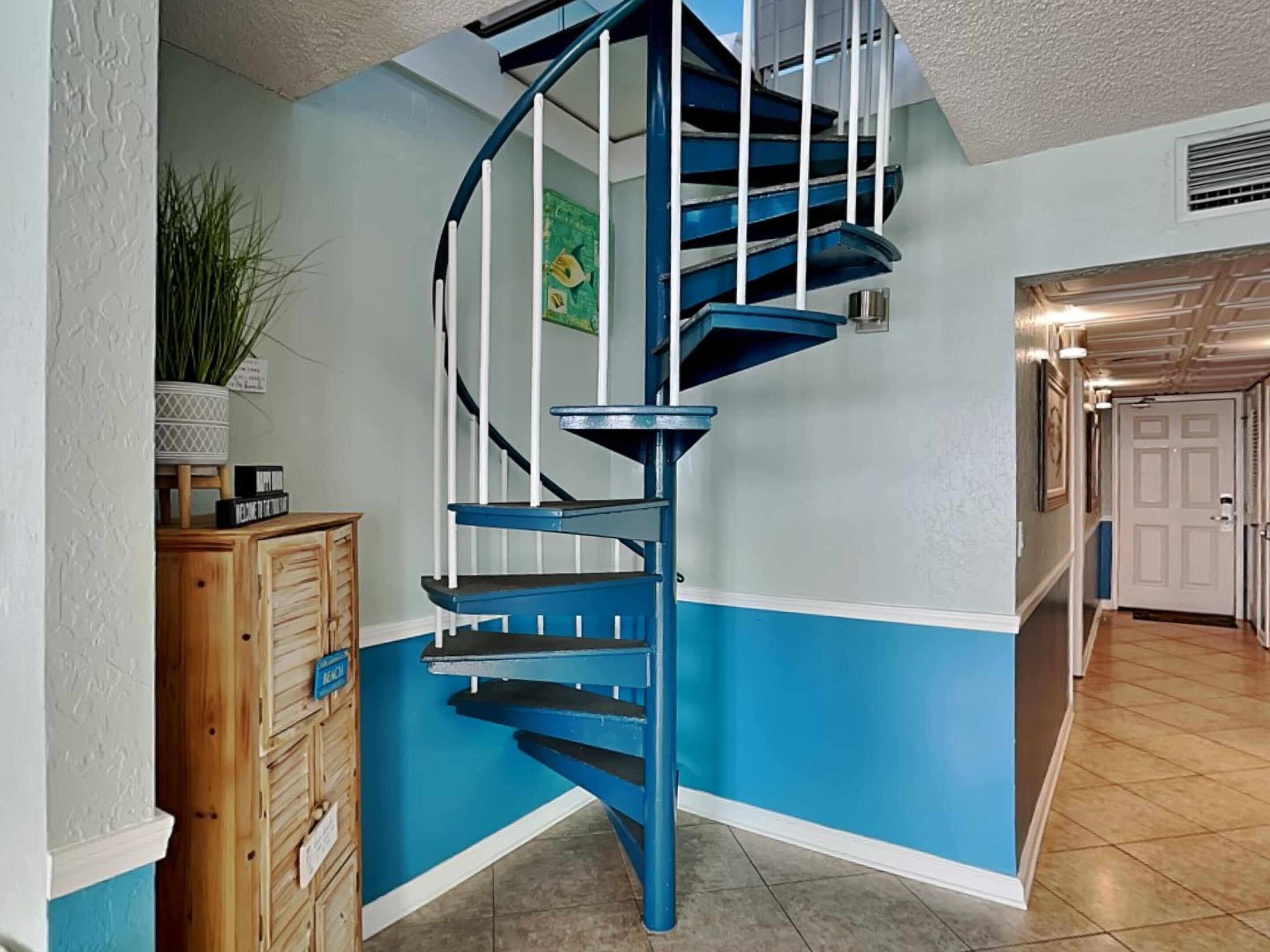 A blue spiral staircase in a hallway with a wooden cabinet and a potted plant.