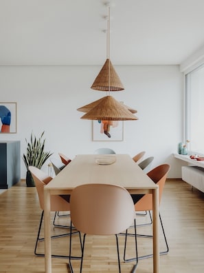 A modern dining area with a wooden table, six chairs, and two hanging wicker lamps.