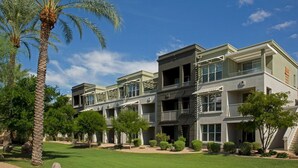 Un hotel de varios pisos con balcones, un césped cuidado y palmeras.