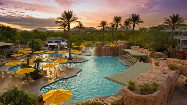 Un área de piscina en un resort, con varias piscinas, sillones de descanso y sombrillas.