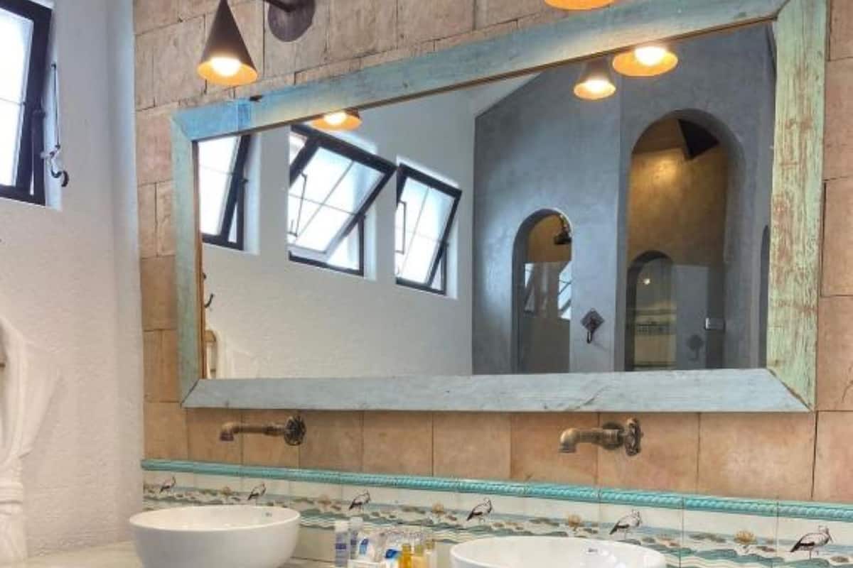 Une salle de bain avec deux lavabos, un grand miroir et un panier en osier.