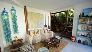 Una sala de estar con sofá, mesa de centro y objetos decorativos. Se ve una escalera que lleva a un nivel superior.