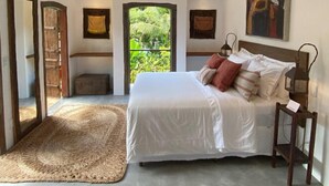 Un dormitorio con una cama grande, un cabecero de madera, un tapiz tejido y vistas a la vegetación a través de una puerta.