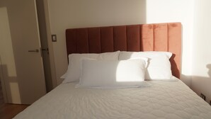 Een net opgemaakt bed met witte lakens en een bruin hoofdbord in een hotelkamer.