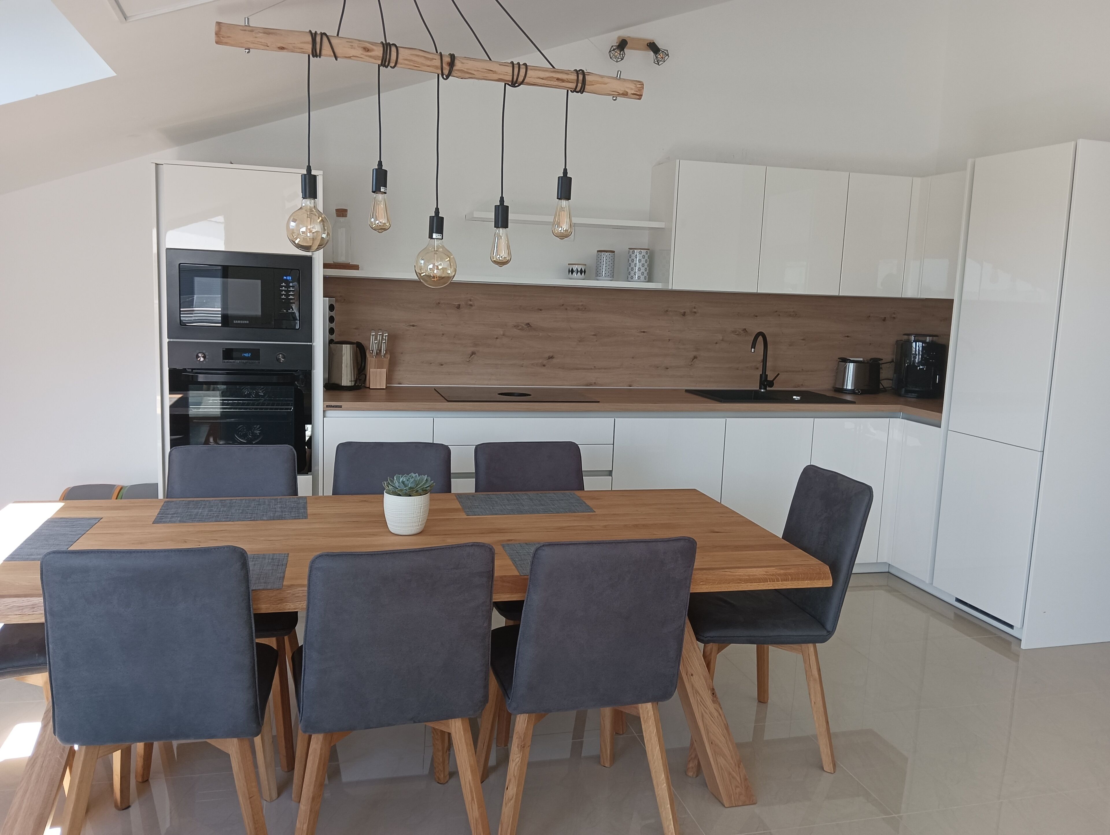 A modern kitchen with white cabinets, a wooden countertop, and a dining area with a wooden table and chairs.