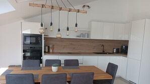 Una cocina moderna con armarios blancos, encimera de madera y una zona de comedor con mesa y sillas de madera.