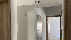 Un pasillo con una puerta de madera, un armario blanco y una cama en la habitación contigua.