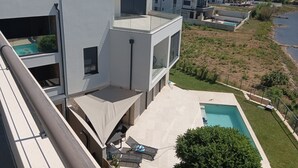 Un moderno edificio residencial con piscina en la azotea, mobiliario exterior y vistas al mar.