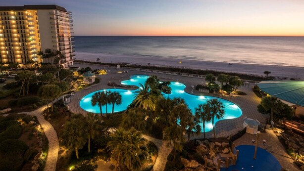 Un resort con una gran piscina iluminada, playa y un hotel de gran altura.