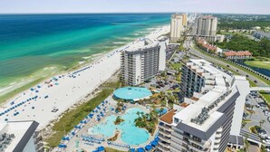 Un hotel costero con varias piscinas, una playa y edificios altos al fondo.