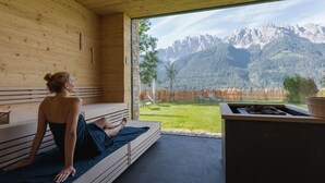 Eine Holzhütte mit Sauna, Blick auf Berge und einer Feuerstelle.
