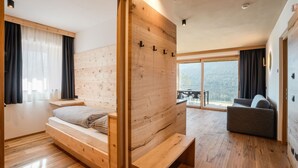Ein modernes Schlafzimmer mit einem hölzernen Bett, einer eingebauten Sitzbank und einem großen Fenster mit Blick ins Freie.