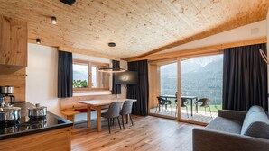 Eine moderne Küche mit Holzboden, einem Essbereich mit Tisch und Stühlen, einer Couch und einer großen Schiebeglastür, die auf eine Terrasse mit Bergblick führt.