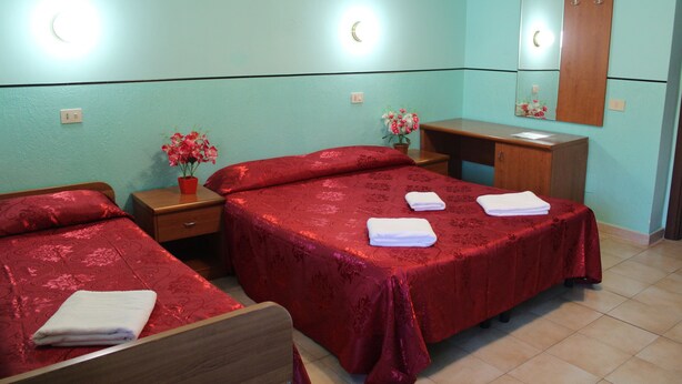 A hotel room with two beds, a desk, a mirror, and a nightstand with a vase of flowers. - Triple Room (Roma)