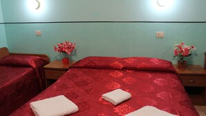 A hotel room with two beds, each with red bedding and floral arrangements. - Triple Room (Roma)