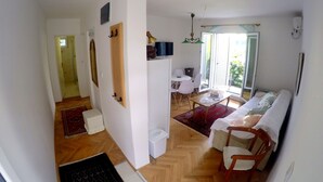 Ein großzügiger Wohnbereich mit einer Couch, einem Esstisch mit Stühlen, einer kleinen Küchenzeile und einer Schiebetür zu einem Außenbalkon.