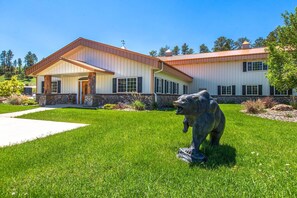 Una casa de dos pisos con cimientos de piedra, un porche delantero y una gran estatua de oso en el jardín.
