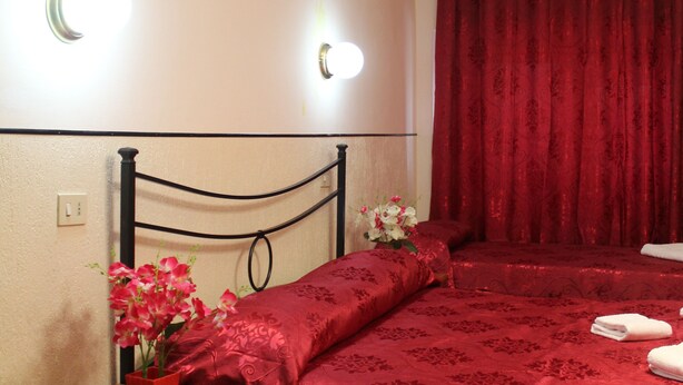 Un dormitorio con cama, mesita de noche, un jarrón con flores y una cortina roja.