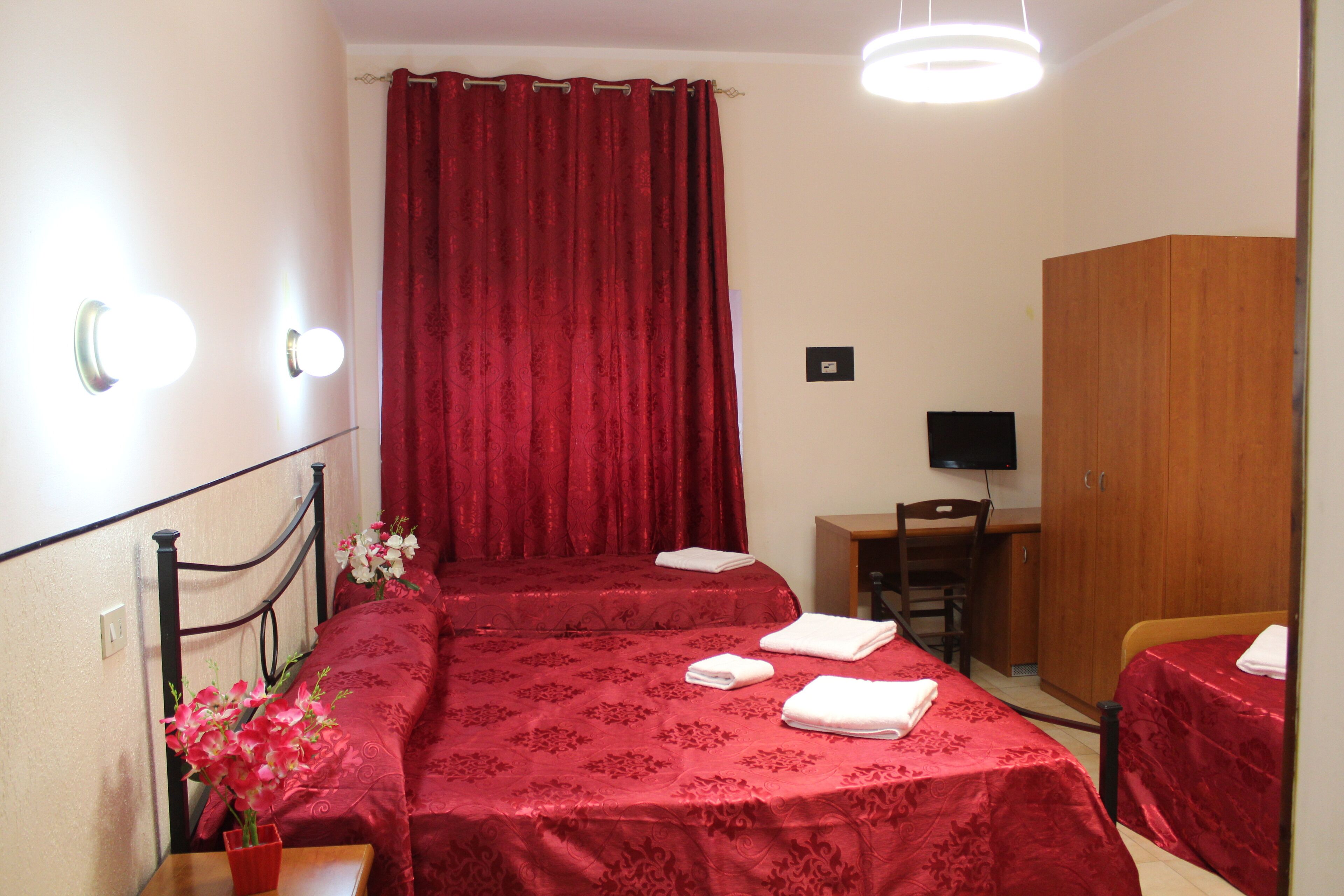 Ein Hotelzimmer mit zwei Betten, einem Schreibtisch, einem Stuhl, einem Kleiderschrank und einem Fernseher.