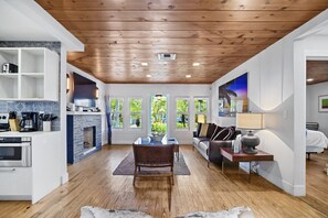 Relax in a spacious open-plan living area with a high ceiling and large windows offering views of lush greenery.
