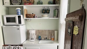 A compact kitchen with a microwave, coffee maker, and a small refrigerator. There are cabinets, a sink, and a note on the door.