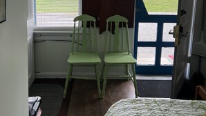 A room with a bed, two green chairs, a wooden cabinet, and a door leading outside.