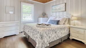 Un dormitori amb sostre de fusta, un llit amb roba de llit floral, una taula de nit, un armari i una finestra amb persianes.