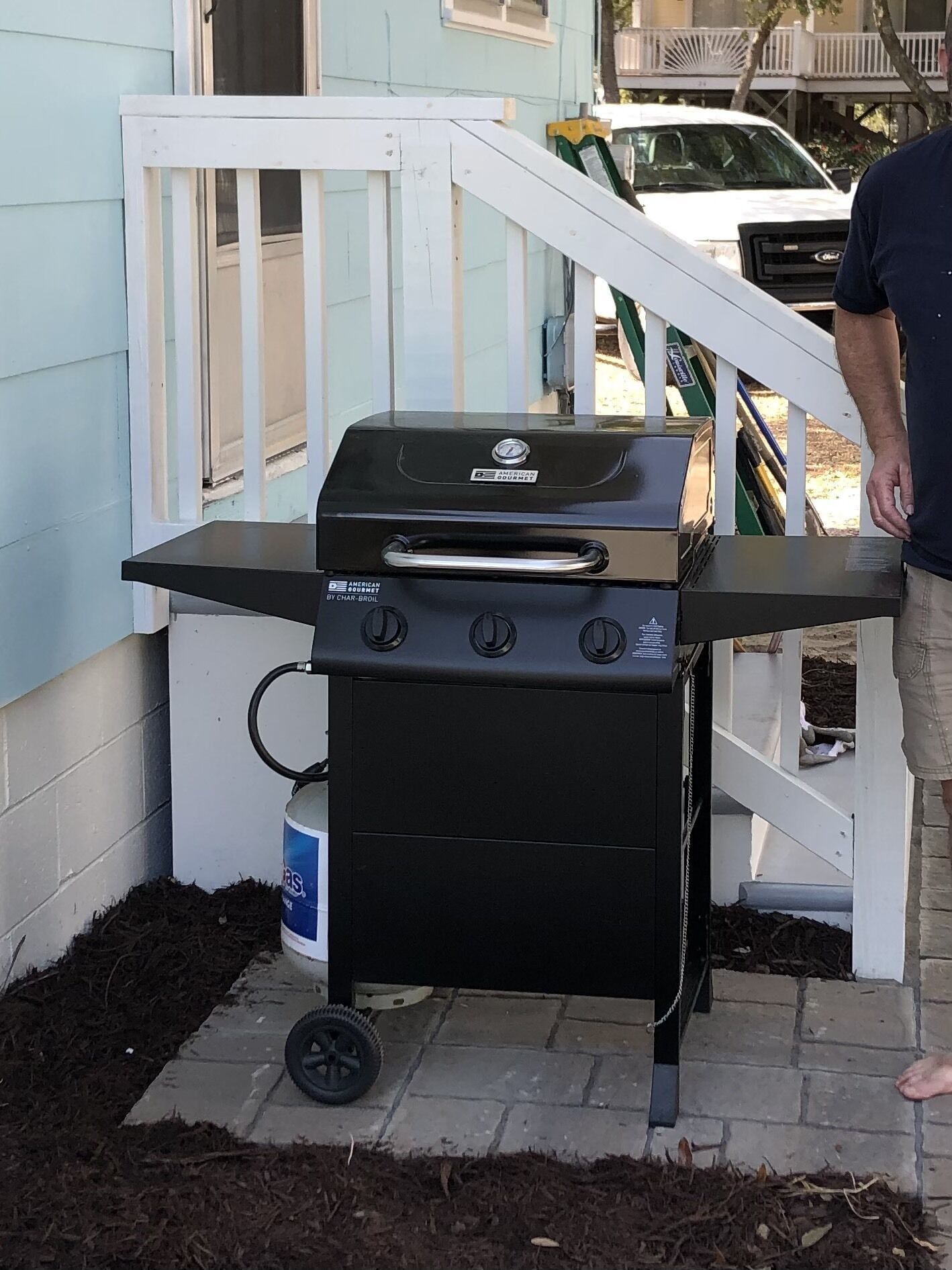 Un barbecue portatif doté de quatre brûleurs et d’une étagère latérale, posé sur une base en briques et muni d’une roue pour faciliter son déplacement.