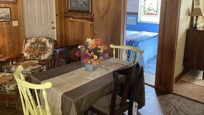 A wooden dining room with a table set for four, chairs, a vase of flowers, and a door with a 'Gone Fishing' sign. - Skip’s Rustic River Cabin near Okefenokee Swamp (Folkston)