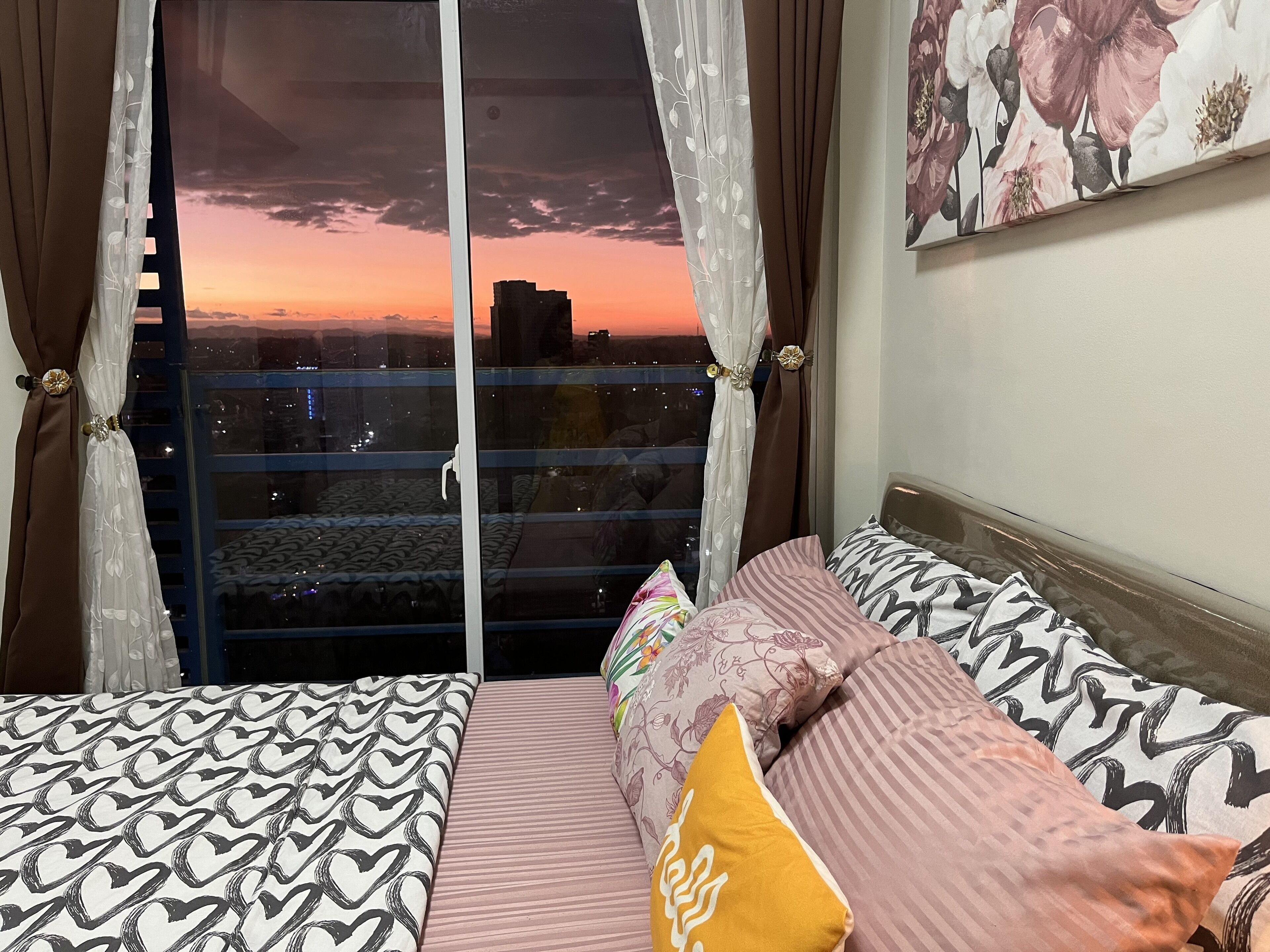 Camera da letto con due letti, vista sulla città al tramonto e balcone con ringhiera.