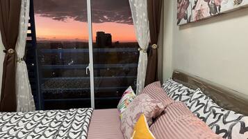 Camera da letto con due letti, vista sulla città al tramonto e balcone con ringhiera.