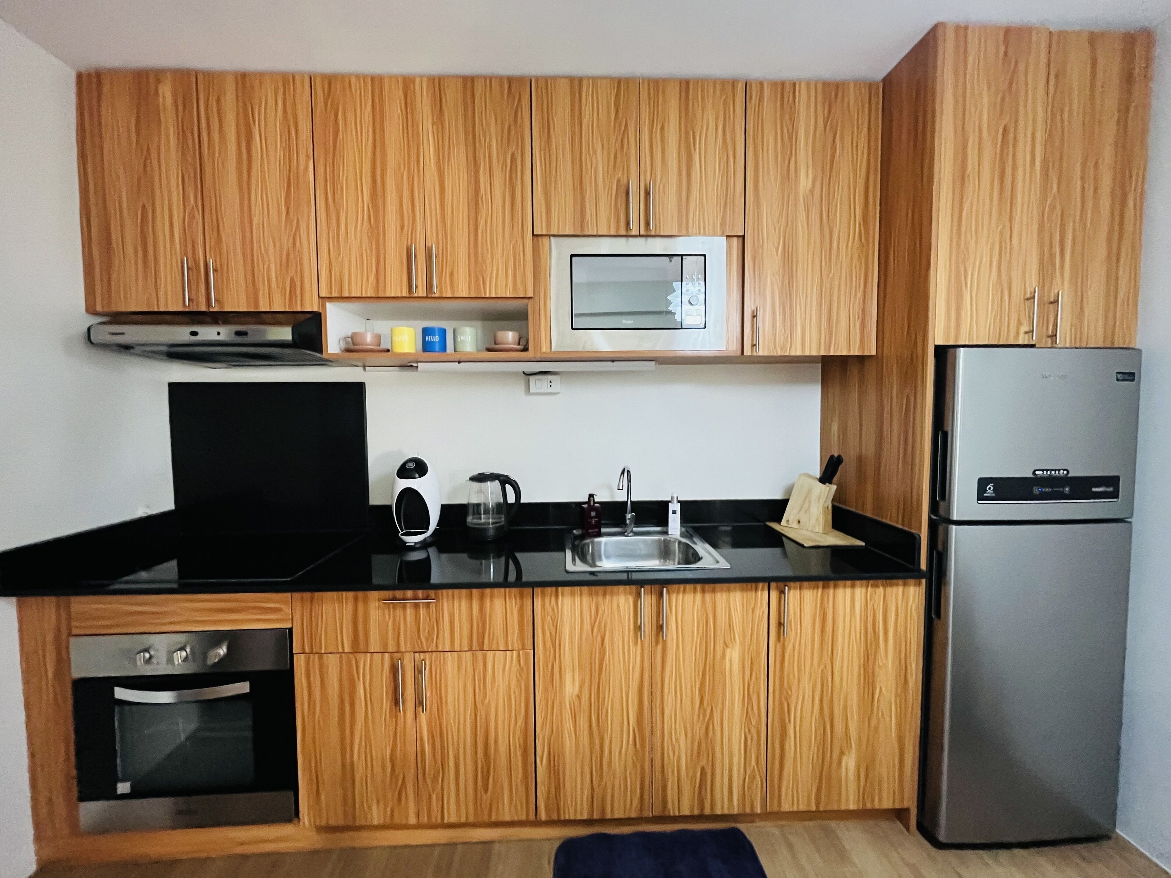 A modern kitchen with wooden cabinets, a stainless steel refrigerator, a microwave, and a sink.