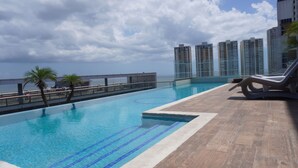 A rooftop infinity pool with clear blue water, a palm tree, and a view of the ocean and high-rise buildings. - Lovely Modern Apartment Two Bedrooms, Two Bathrooms, Nice Location (Panamá)