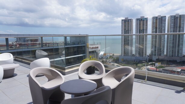 A rooftop terrace with modern chairs and tables, overlooking a cityscape and the sea. - Lovely Modern Apartment Two Bedrooms, Two Bathrooms, Nice Location (Panamá)