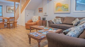 Un salon avec un escalier en bois, un canapé, une table basse avec des magazines et un tableau au mur.