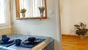 Un coin repas avec une table dressée pour deux personnes, une fenêtre avec des rideaux et un plancher en bois.