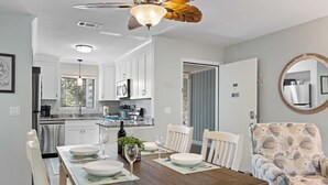 A dining area with a wooden table, white chairs, and a floral-patterned armchair. - Amazing Lagoon View, Largest Balcony in Fiddlers Cove!  5 min walk to the beach! (Hilton Head Island)