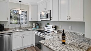 A modern kitchen with white cabinets, a stainless steel dishwasher, a built-in oven, and a granite countertop. - Amazing Lagoon View, Largest Balcony in Fiddlers Cove!  5 min walk to the beach! (Hilton Head Island)
