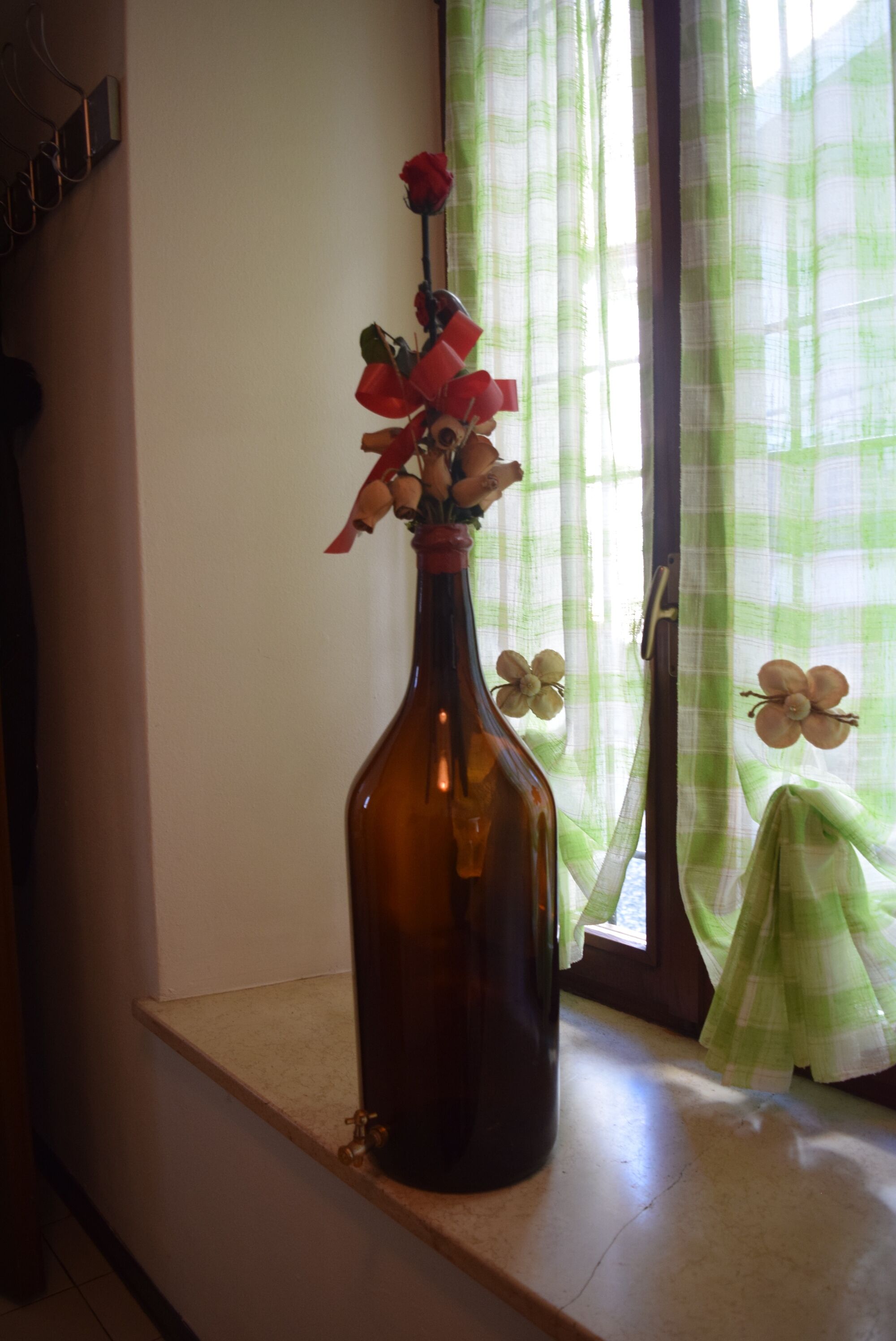 Eine braune Flasche mit einer roten Blumenkomposition auf einem Fensterbrett.