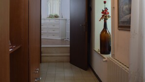 Un couloir avec une armoire en bois, une commode blanche, un vase de fleurs et un tableau accroché au mur.