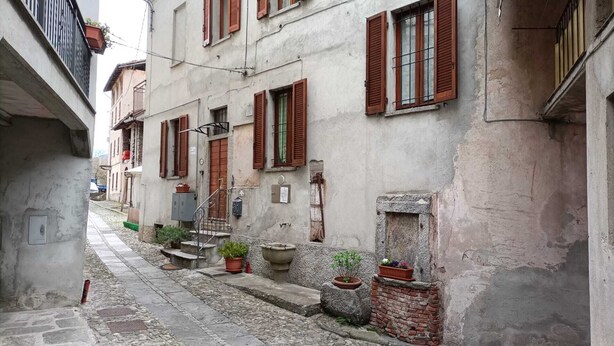 Une ruelle étroite pavée, bordée d’immeubles à l’architecture traditionnelle, avec des volets en bois et des plantes en pot.