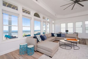 A spacious living room with a large sectional sofa, a round coffee table, and a view of the ocean through large windows. - New!! Stunning Gulf Front, private pool, sleeps 16 (Port St. Joe)