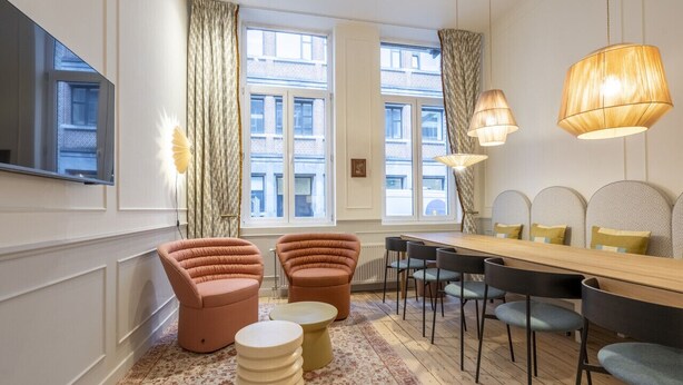 Een moderne woonkamer met een bank, voetenbankje, eettafel, stoelen en een televisie.