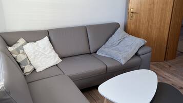 Ein modernes Wohnzimmer mit einem grauen Ecksofa, einem weißen Couchtisch und einer Holztür.