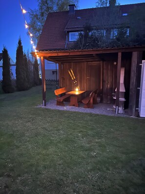 Un espace extérieur aménagé en bois, avec des bancs et une table, entouré d’une pergola en bois.